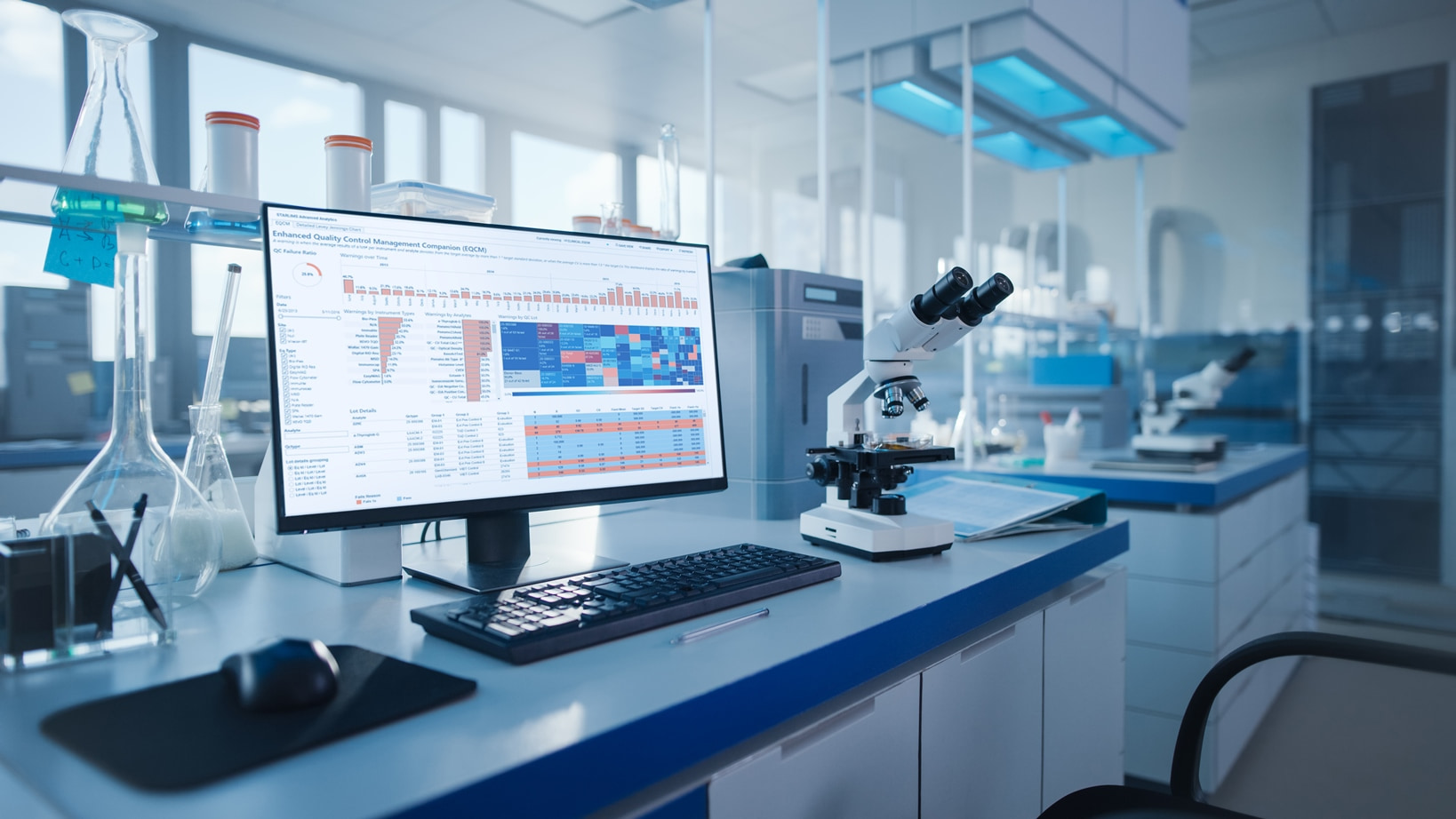 A monitor on a laboratory desk shows STARLIMS Advanced Analytics reporting and data visualizations